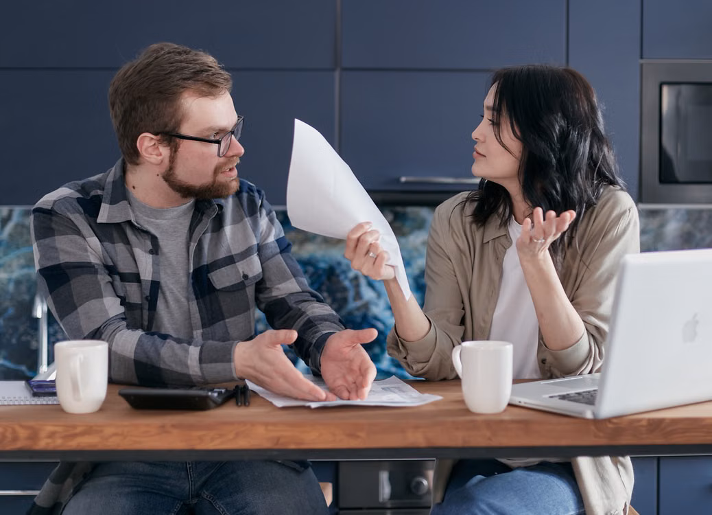 Two adults discussing a document beside an open laptop.