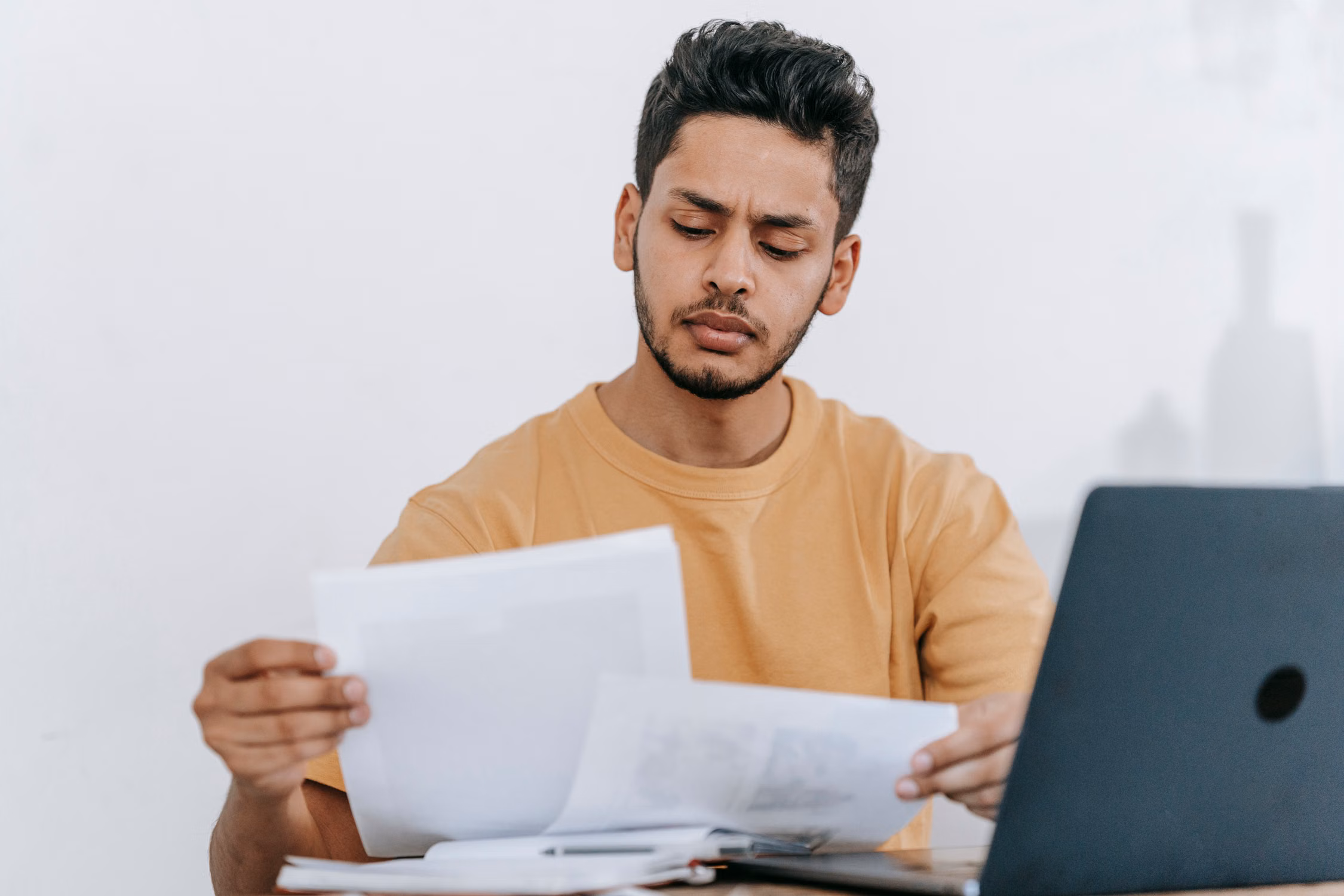 A man considering documents beside his laptop