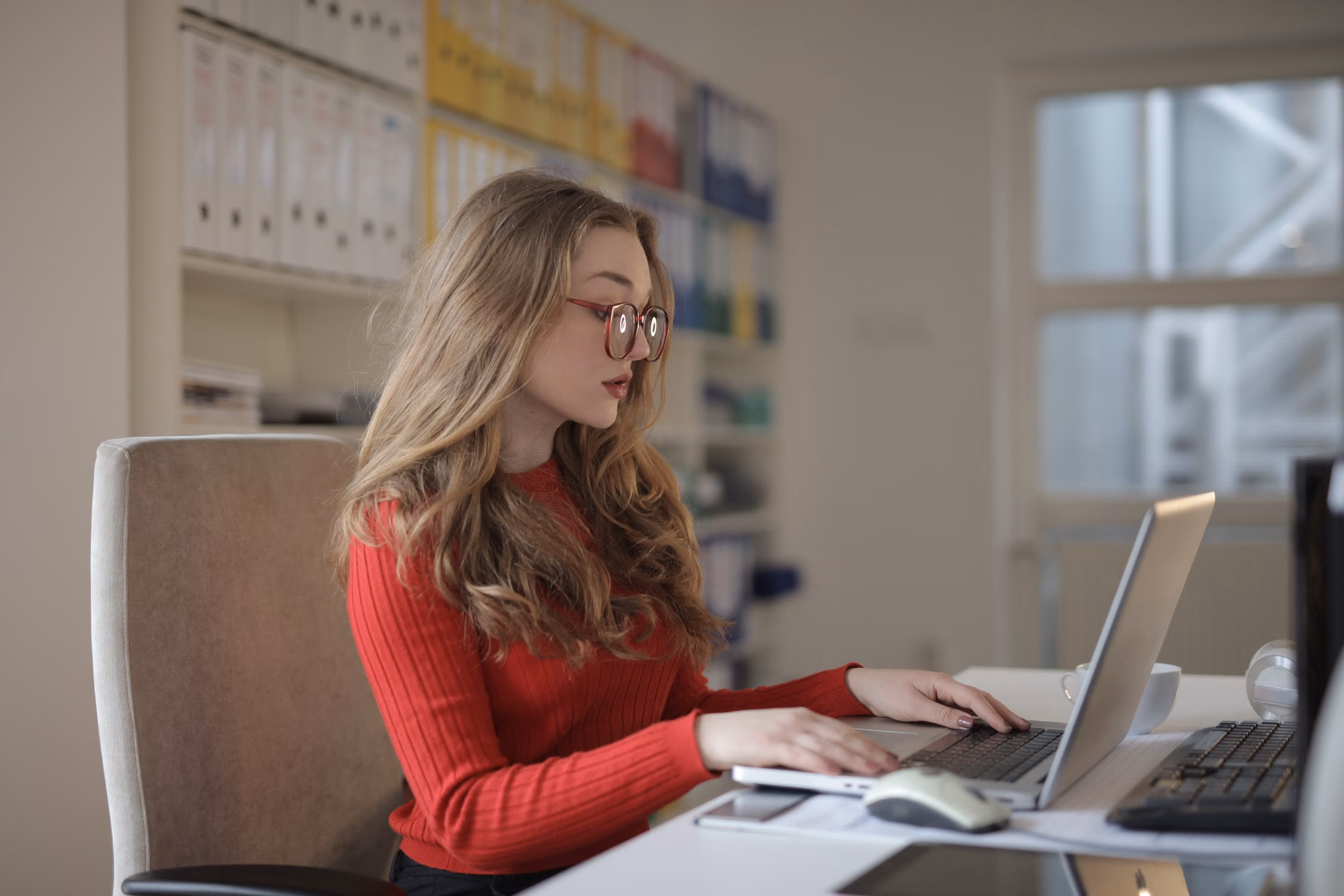 A woman wearing glasses while working at a laptop