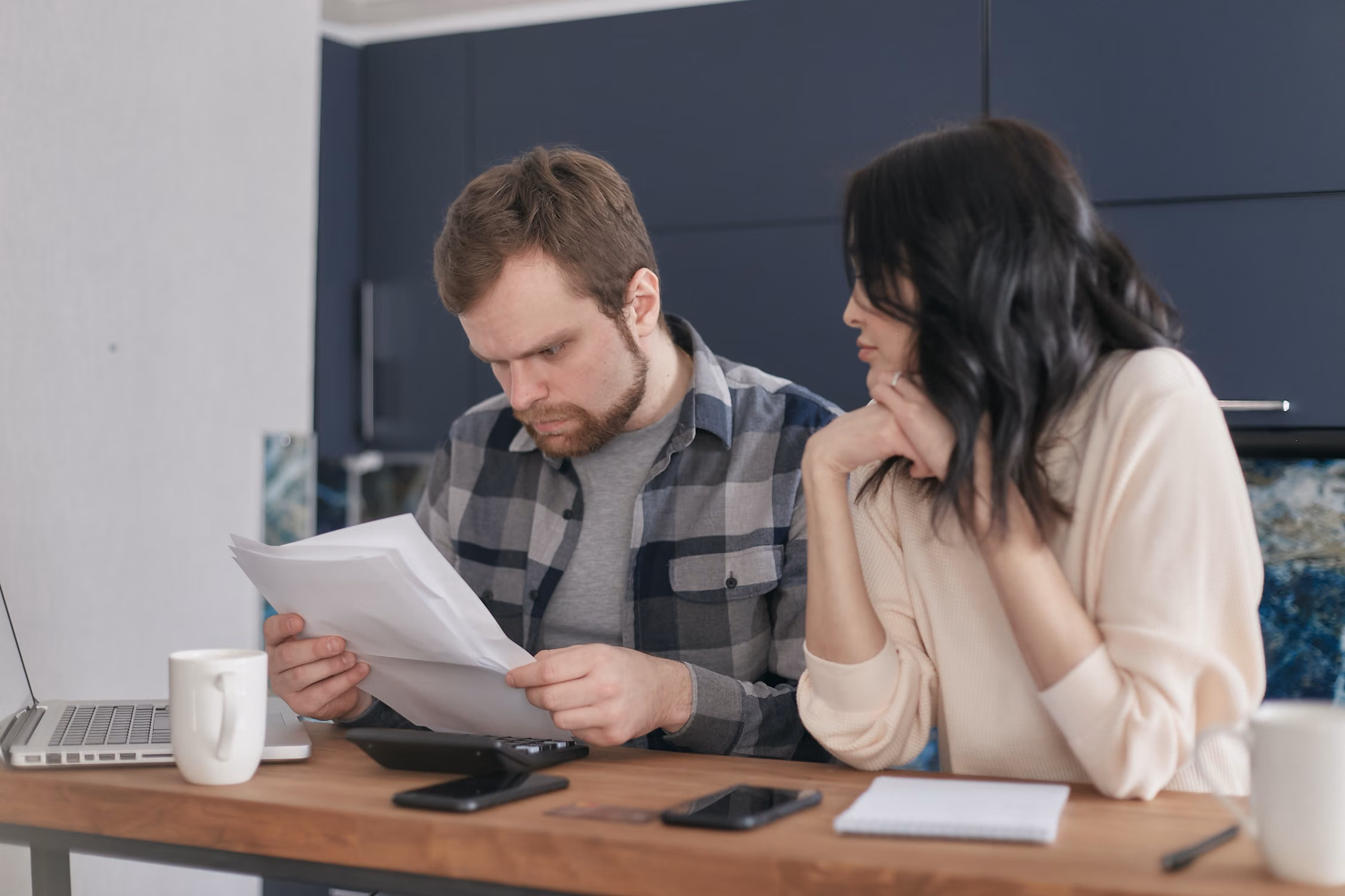 A couple comparing bills and paperwork beside a laptop